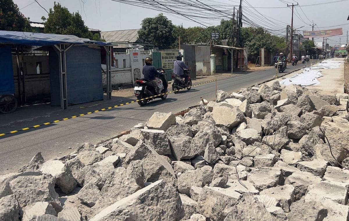 Permukaan Jalan Pisangan di Pakuhaji tampak dibongkar, menyisakan hamparan tanah dan material proyek perbaikan.