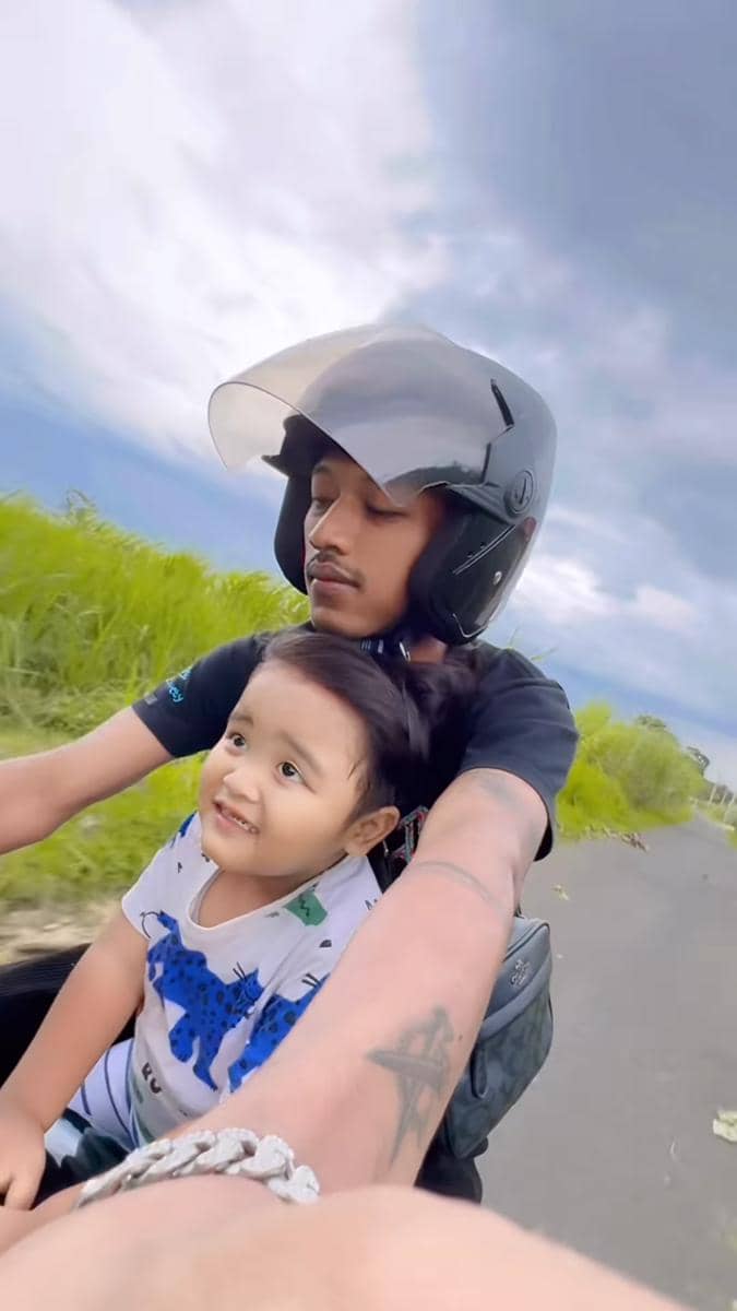 Koko Seto menggendong seorang anak kecil sambil tersenyum dalam momen pengasuhan yang hangat dan akrab.