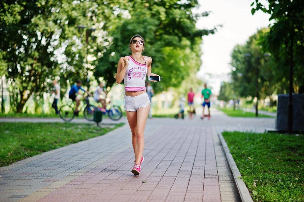 Ilustrasi perempuan berambut panjang mengenakan pakaian olahraga sedang jogging di jalur taman dengan latar pepohonan.
