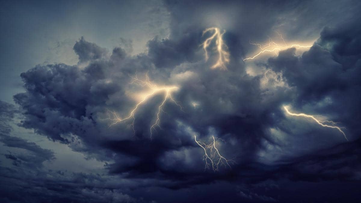 Sambaran petir bercabang melintas di langit malam yang berawan gelap, memancarkan cahaya terang di antara awan.