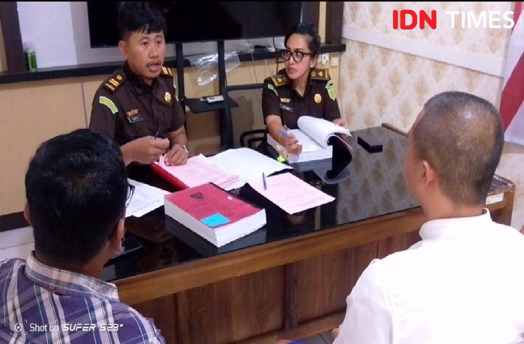 Seorang tersangka berbaju putih membelakangi kamera saat tiba untuk pelimpahan perkara, disaksikan petugas Kejaksaan Banyumas.