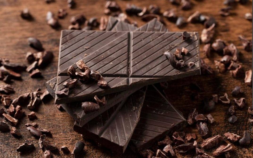 Ilustrasi potongan dark chocolate compound berwarna cokelat gelap dengan tekstur padat untuk bahan olahan makanan.