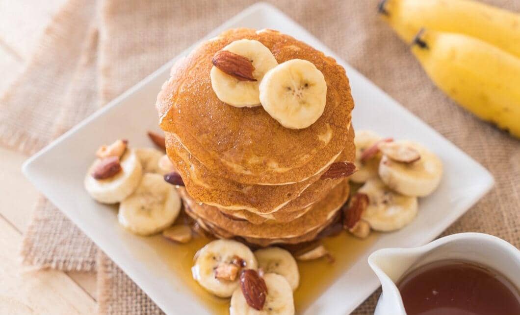Sepiring pancake pisang madu dengan irisan pisang dan siraman madu, disajikan sebagai menu sarapan manis.