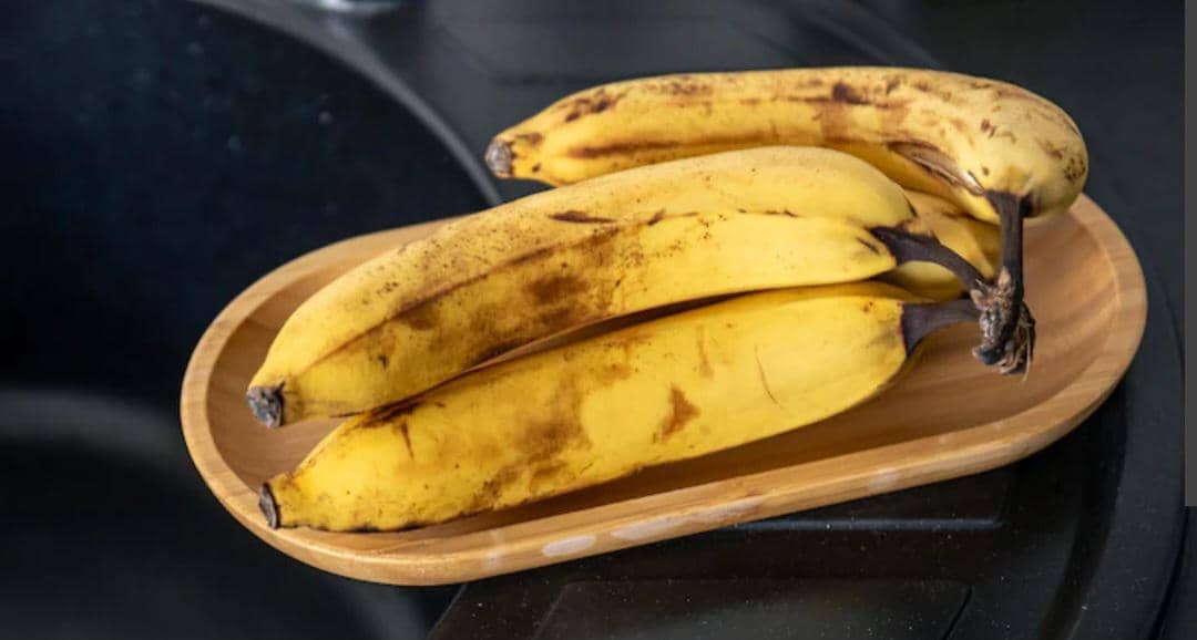 Sekelompok pisang matang berwarna kuning dengan beberapa bintik cokelat tersusun di atas permukaan putih.