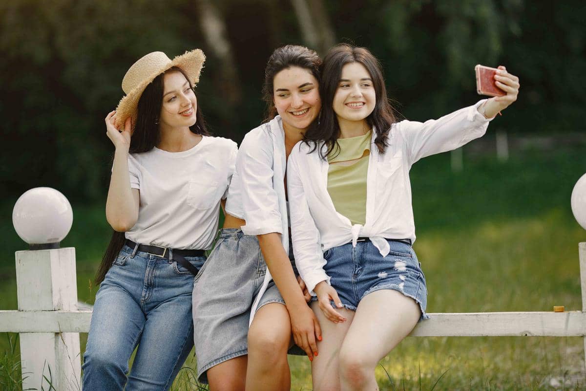 Sekelompok teman berpose untuk swafoto di taman, dengan seorang perempuan mengenakan topi dan kaus putih di depan.