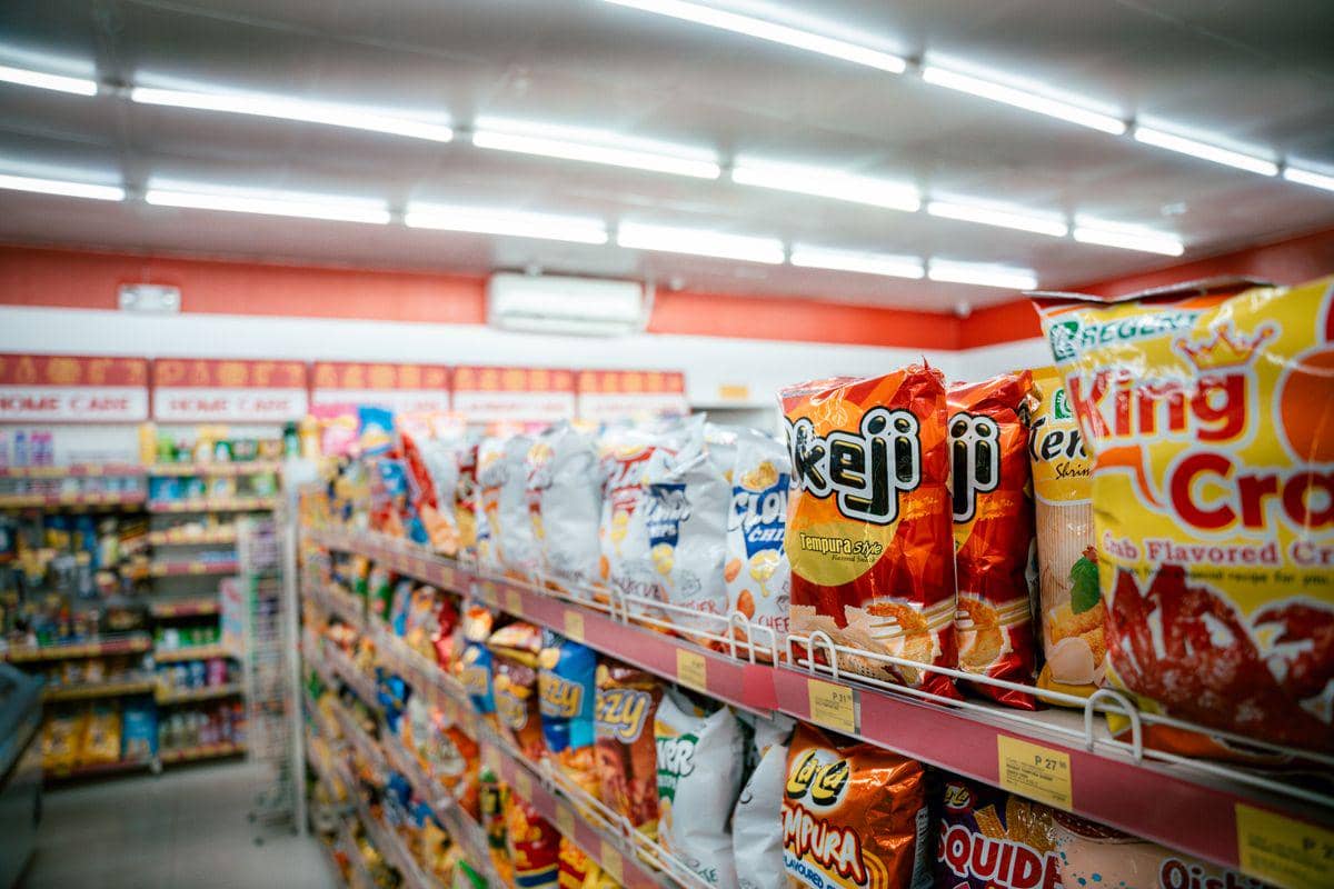Deretan label harga elektronik berwarna kuning dan putih pada rak produk di supermarket dengan latar lorong belanja.