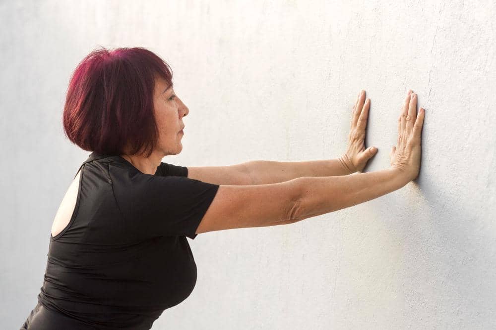 Ilustrasi seseorang melakukan wall push-up dengan kedua tangan bertumpu pada dinding sebagai latihan kekuatan tubuh.