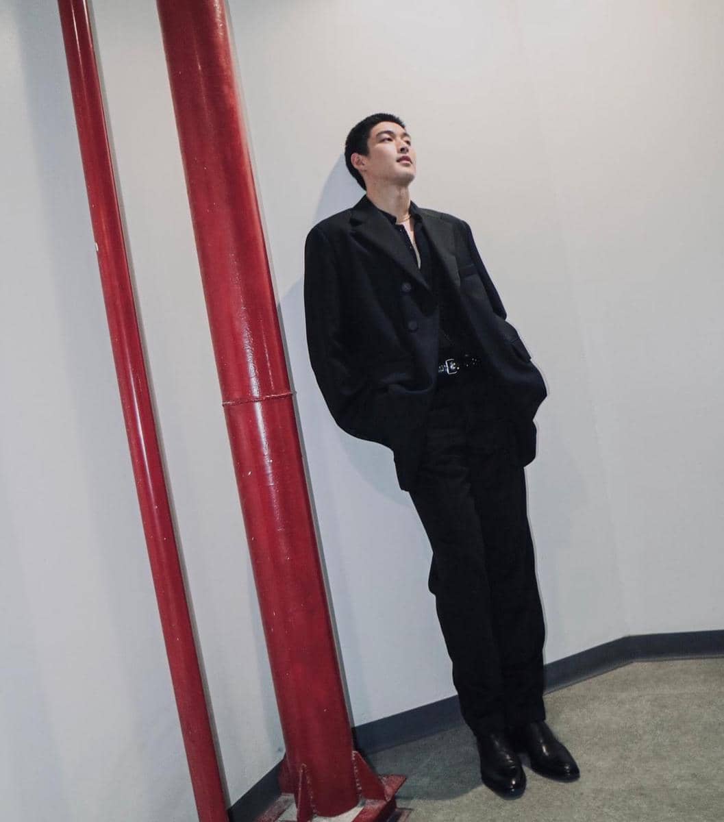 Krating Khunnarong berpose mengenakan setelan jas sebagai inspirasi OOTD formal bergaya rapi dan modern.