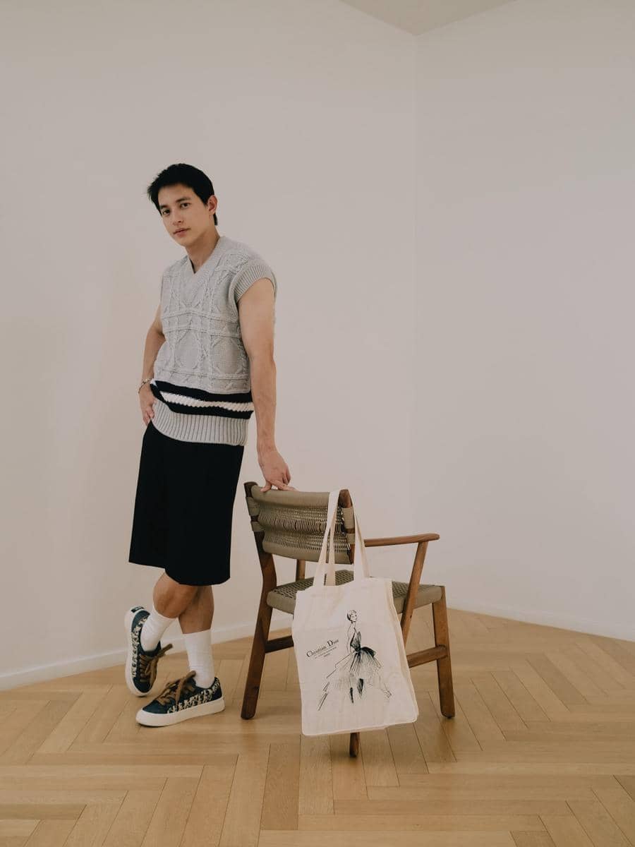 James Jirayu tampil kasual dalam OOTD bernuansa gelap dengan sepatu kets, berpose di area luar ruangan.