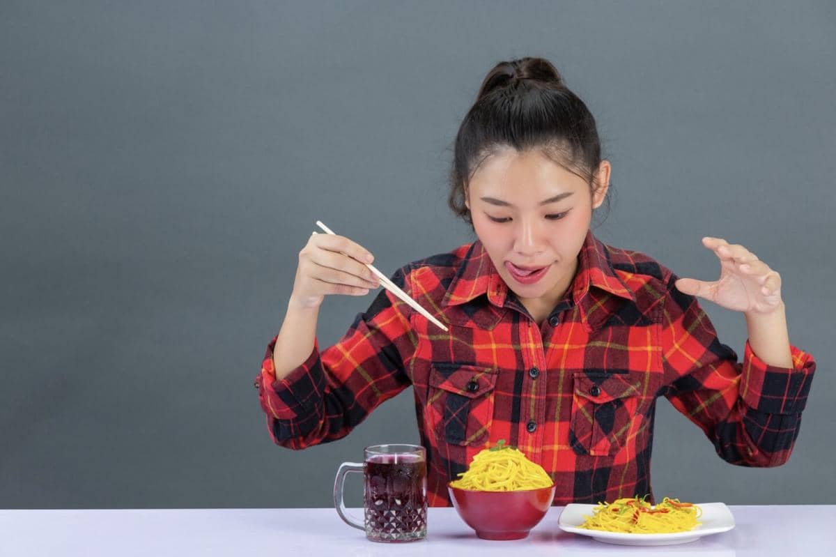 Ilustrasi seorang perempuan duduk di meja dengan makanan cepat saji, camilan, dan minuman untuk menggambarkan pola makan berantakan.