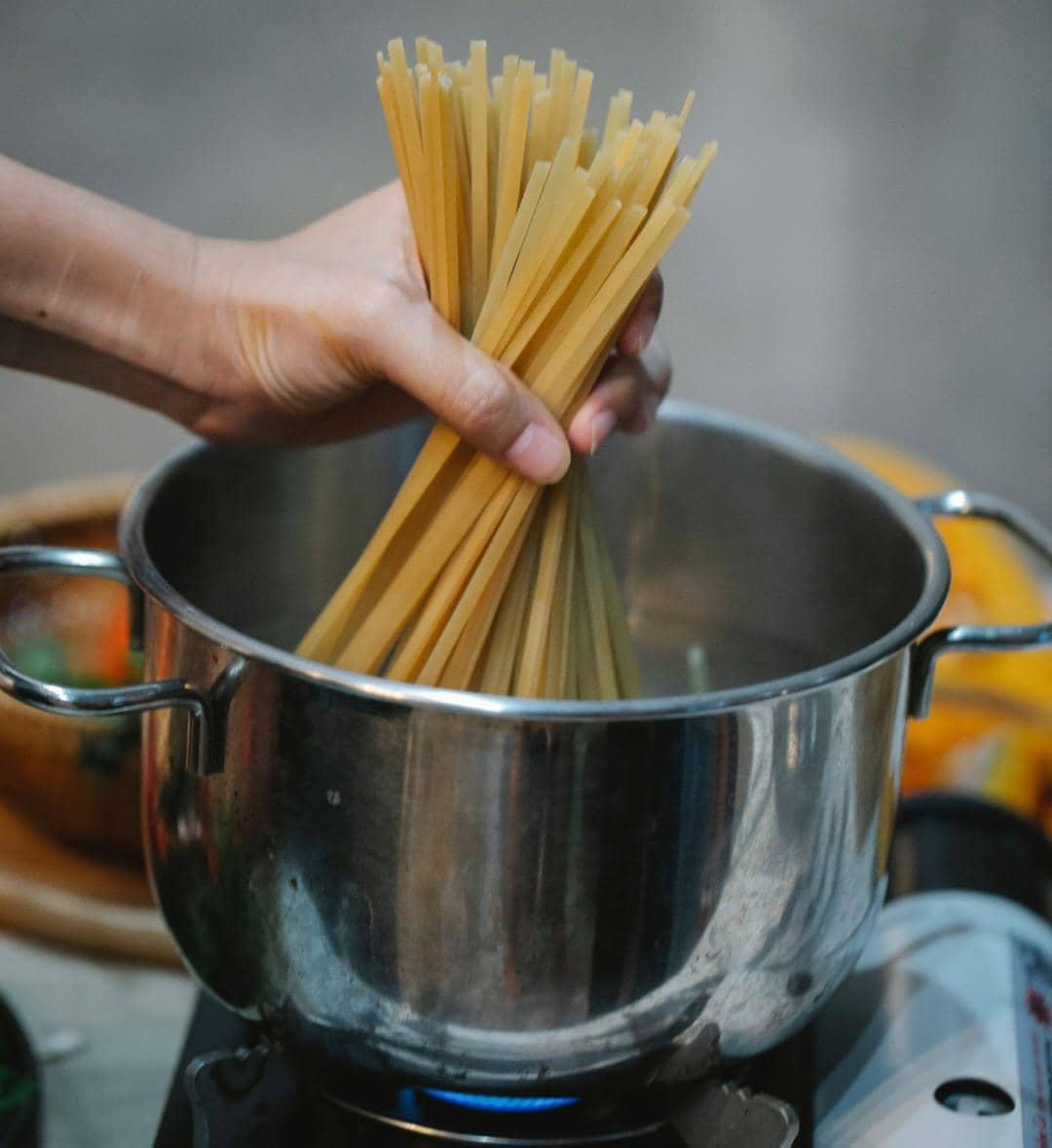 Tangan menggunakan penjepit untuk mengaduk spaghetti yang direbus dalam panci berisi air mendidih di atas kompor.
