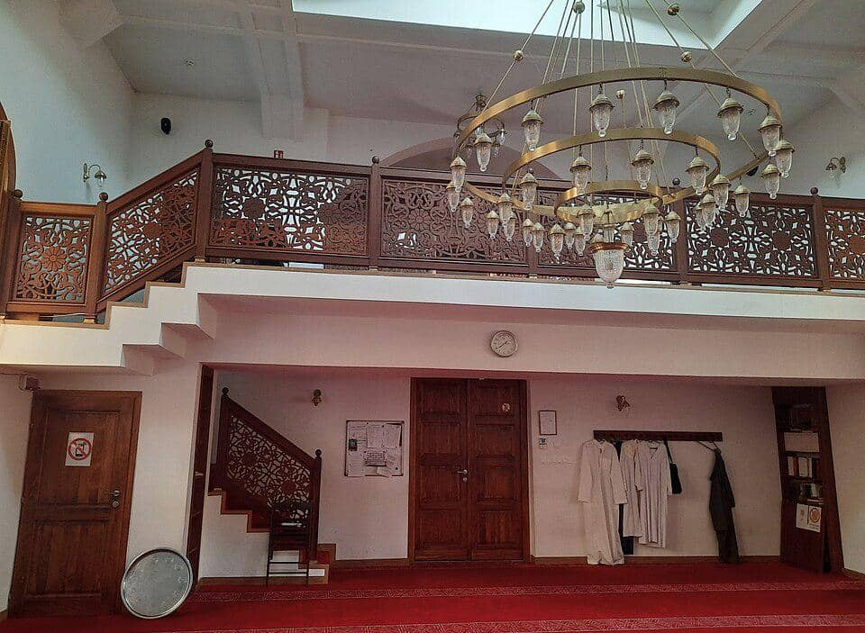 Aula salat di dalam Masjid Kaunas dengan lampu gantung yang menggantung di tengah ruangan, menerangi interior masjid.