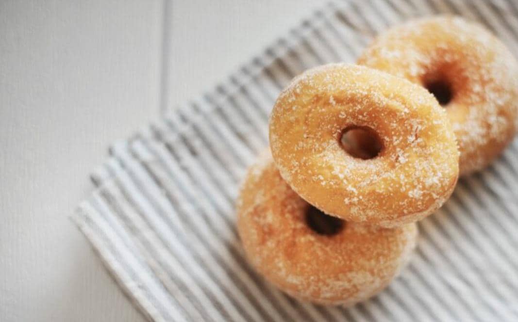 Donat gula berwarna cokelat keemasan bertabur gula halus, disajikan sebagai camilan manis di atas piring.