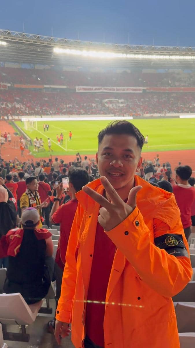 Seorang pria berkaus putih berpose di tribun Stadion GBK saat menyaksikan laga Persija melawan Persib.