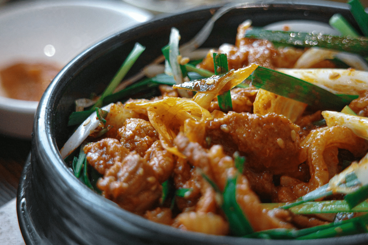 Semangkuk nasi ayam sotbap Korea dengan potongan ayam, telur rebus, dan sayuran hijau di atas meja kayu.