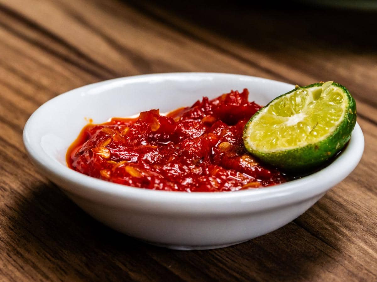 Semangkuk sambal merah bertekstur kasar disajikan di atas meja sebagai pelengkap hidangan tradisional.