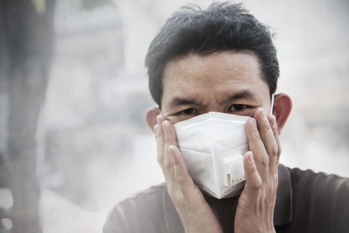 Ilustrasi warga memakai masker berjalan di kawasan perkotaan dengan polusi udara, debu, dan asap pekat.