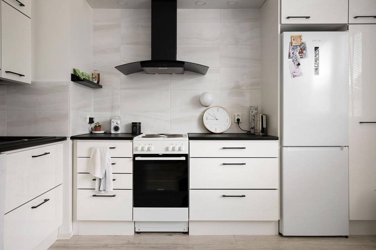 Interior dapur modern dengan kulkas berwarna gelap, kabinet kayu, meja dapur, dan pencahayaan alami dari jendela.
