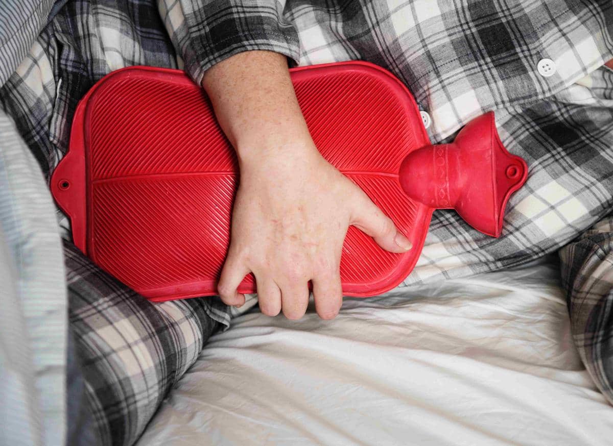 Ilustrasi perempuan menggunakan bantal pemanas pada punggung yang membantu meredakan nyeri haid.