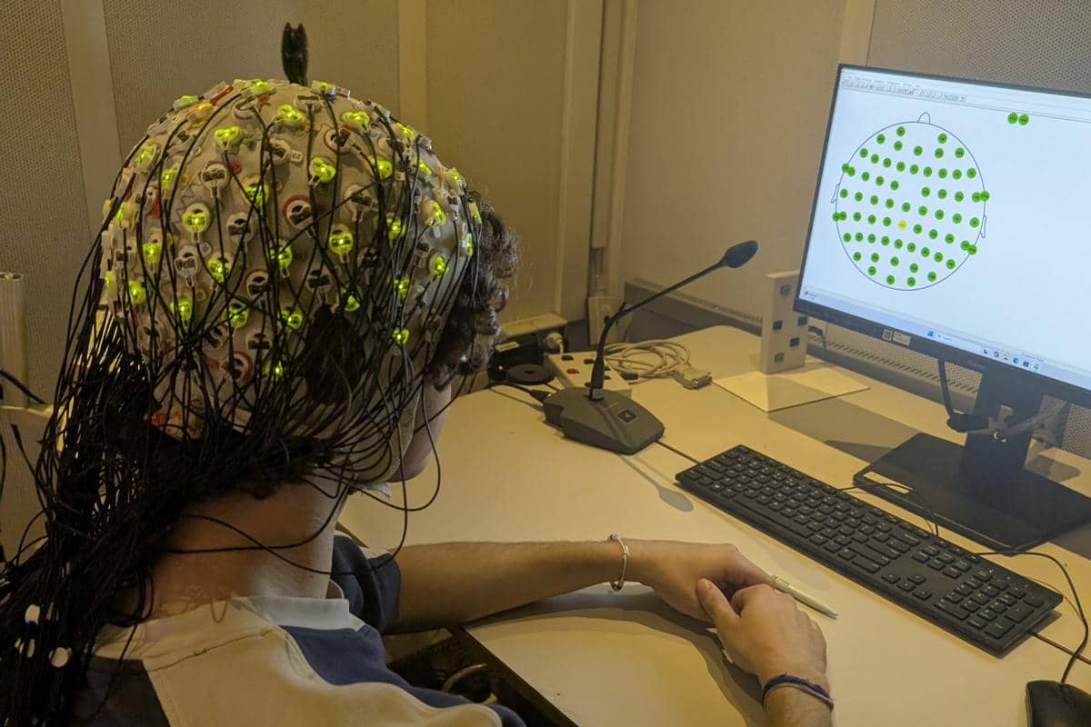 Seorang peserta eksperimen EEG mengenakan penutup kepala dengan elektroda sambil duduk untuk merekam aktivitas otak.