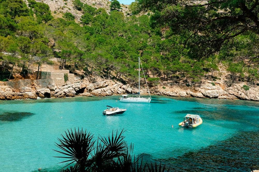 Pemandangan Cala Figuera, teluk berbatu dengan air laut biru, perahu kecil, dan bangunan di pesisir Mallorca.