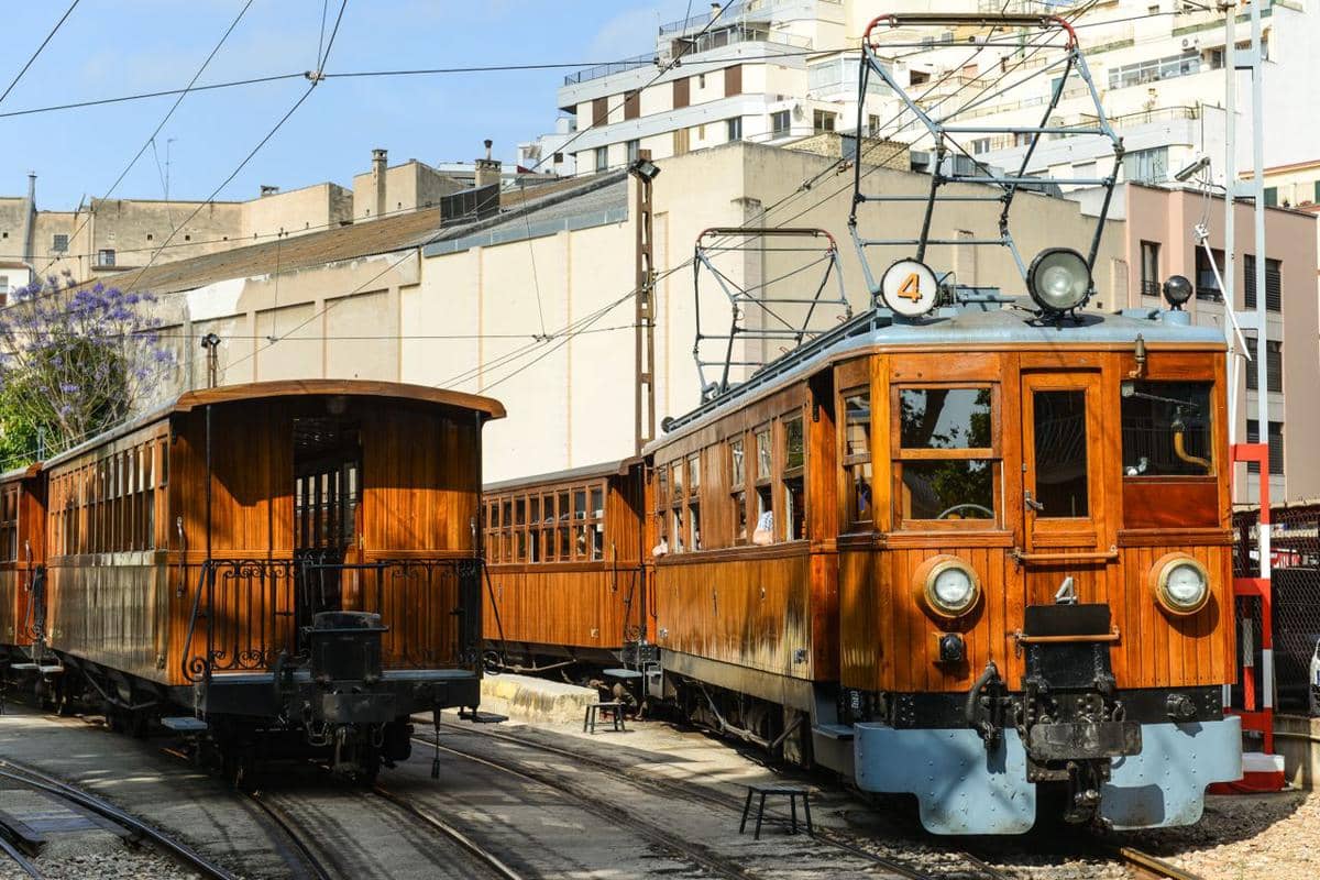 Kereta vintage Tren de Soller melaju di jalur rel Mallorca, Spanyol, dengan lanskap pegunungan di sekitarnya.