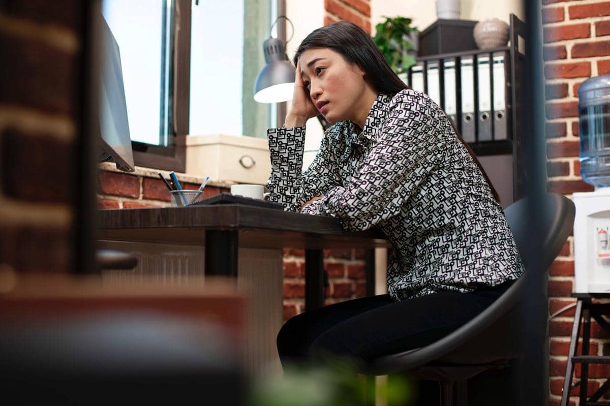 Seorang karyawan tampak lelah menatap laptop di meja kerja sambil memikirkan urusan pribadi yang mengganggu konsentrasi.