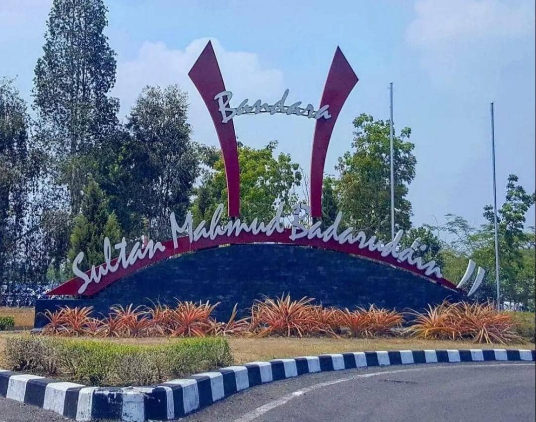 Tampak depan gedung terminal Bandara Sultan Mahmud Badaruddin II di Palembang dengan area jalan dan pepohonan.