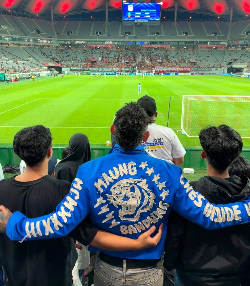 Ganindra Bimo mengenakan jersey Persib saat mendukung klub tersebut di Seoul, Korea Selatan, dengan latar area stadion.