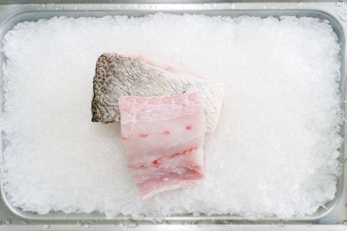 Potongan fillet ikan kakap mentah berwarna pucat disiapkan sebagai bahan utama untuk berbagai olahan hidangan laut.