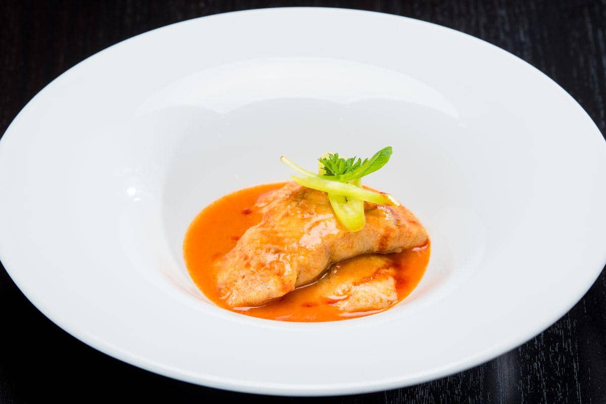 Sepiring fillet kakap asam manis dengan saus merah, sayuran, dan irisan lemon sebagai ilustrasi hidangan.