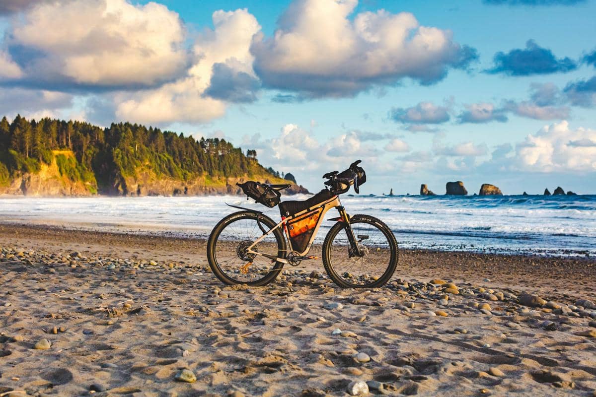 Ilustrasi sepeda terparkir di tepi pantai dengan latar pemandangan tebing karang