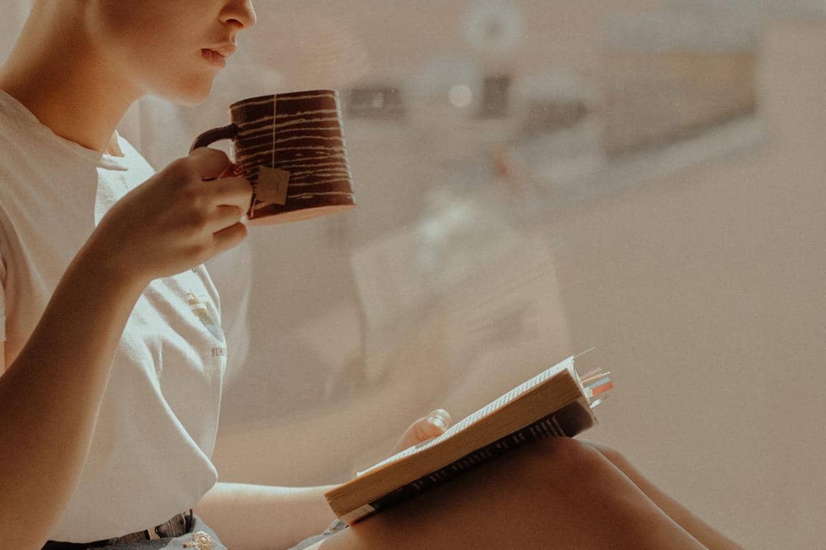 seorang wanita membaca buku sambil minum teh