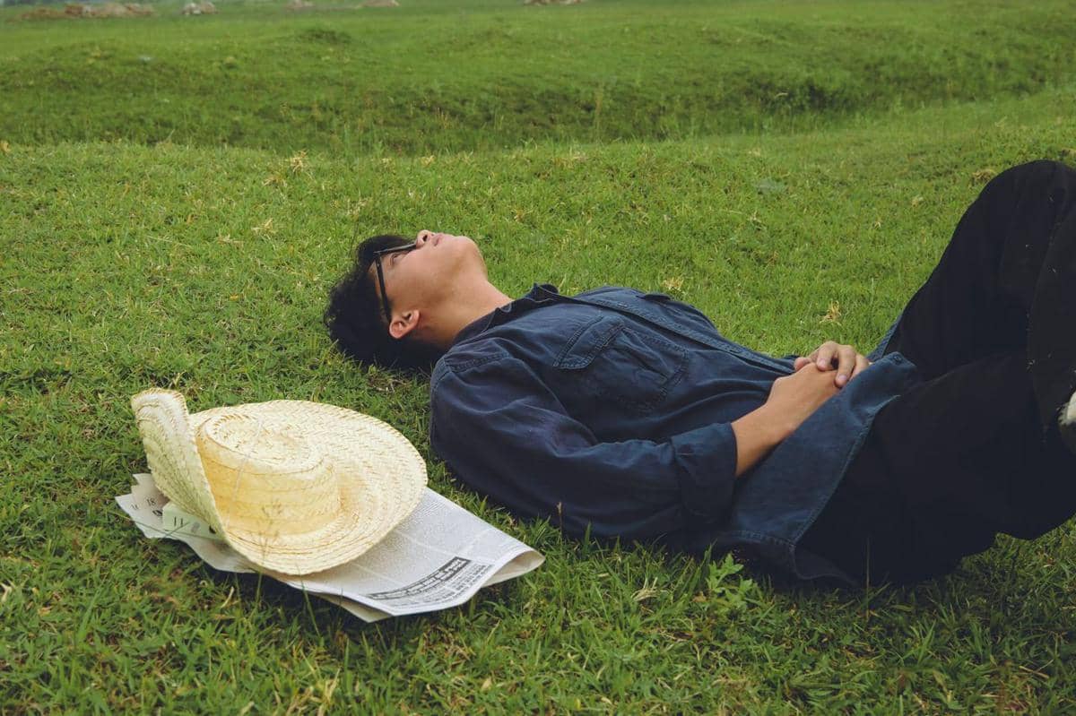 Seorang pria berbaring dengan tangan di bawah kepala, menggambarkan suasana istirahat atau relaksasi.