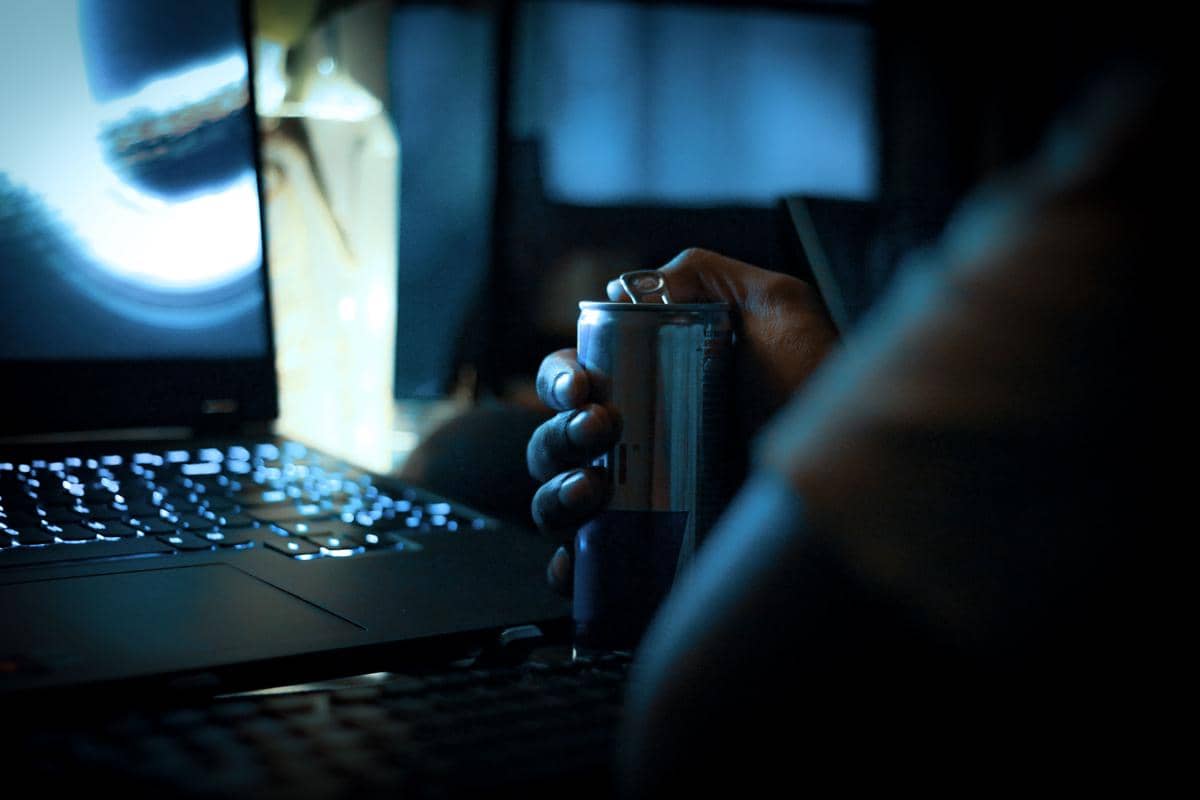 Ilustrasi seseorang bekerja dengan laptop hingga larut malam di meja kerja, ditemani cahaya lampu dalam suasana gelap.