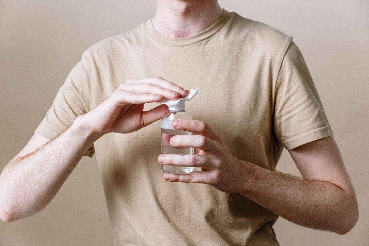 Seorang pria memegang botol cairan pembersih kulit dengan latar polos.