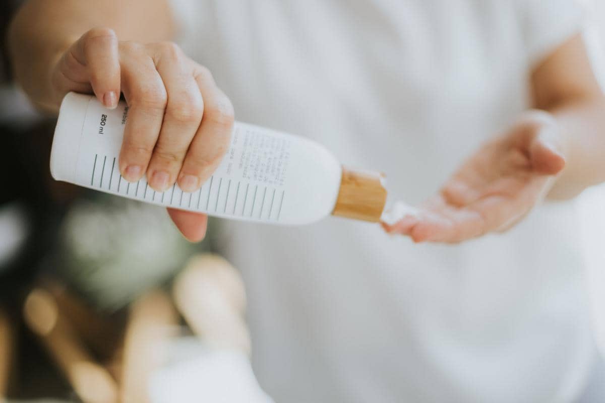 Tangan seseorang sedang menuangkan lotion dari botol putih ke telapak tangan