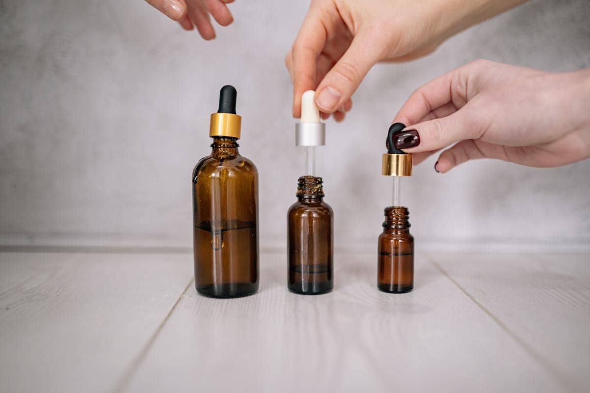 Tangan yang sedang memegang pipet botol serum kaca di atas meja.