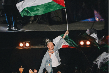 Macklemore tampil di atas panggung sambil mengangkat bendera Palestina saat Paléo Festival Nyon di Swiss pada 2025.