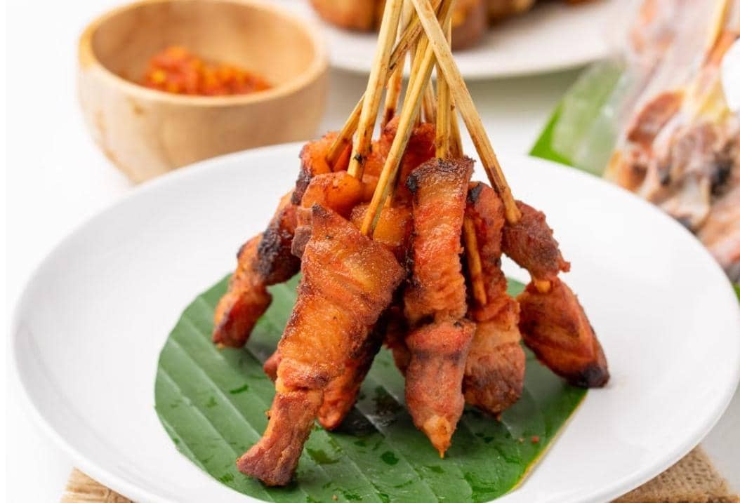 Sepiring sate kambing matang tersusun pada tusuk sate, disajikan dengan irisan bawang merah dan sambal.