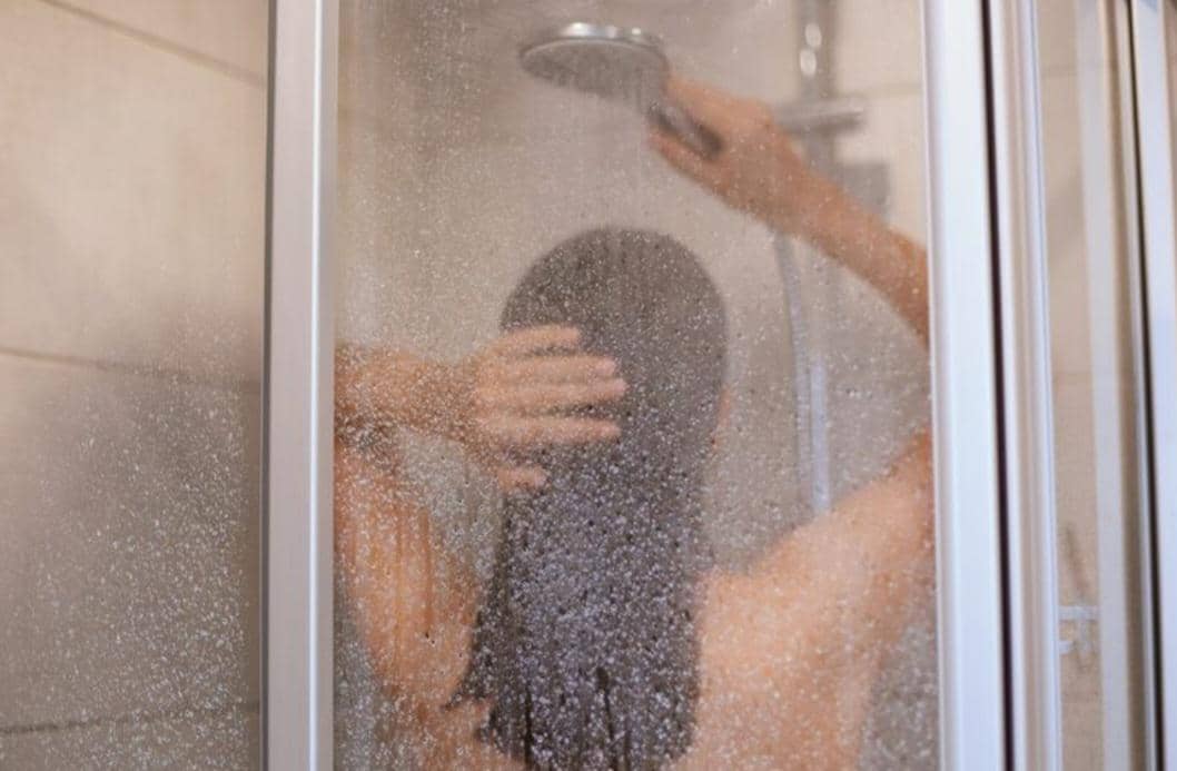 Seseorang mandi menggunakan shower di kamar mandi sebagai bagian dari rutinitas kebersihan diri sehari-hari.
