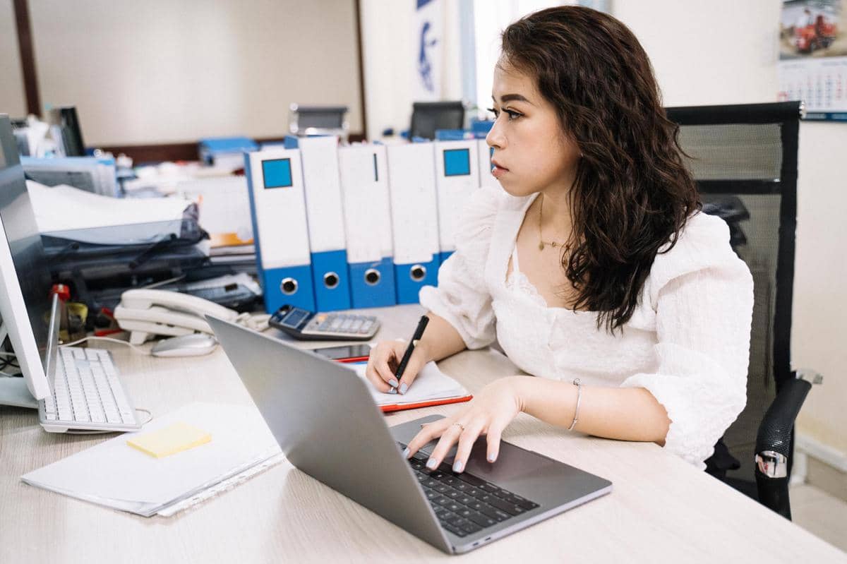 Ilustrasi seorang wanita fokus mengerjakan pekerjaan kantor di meja kerja dalam suasana profesional yang rapi.