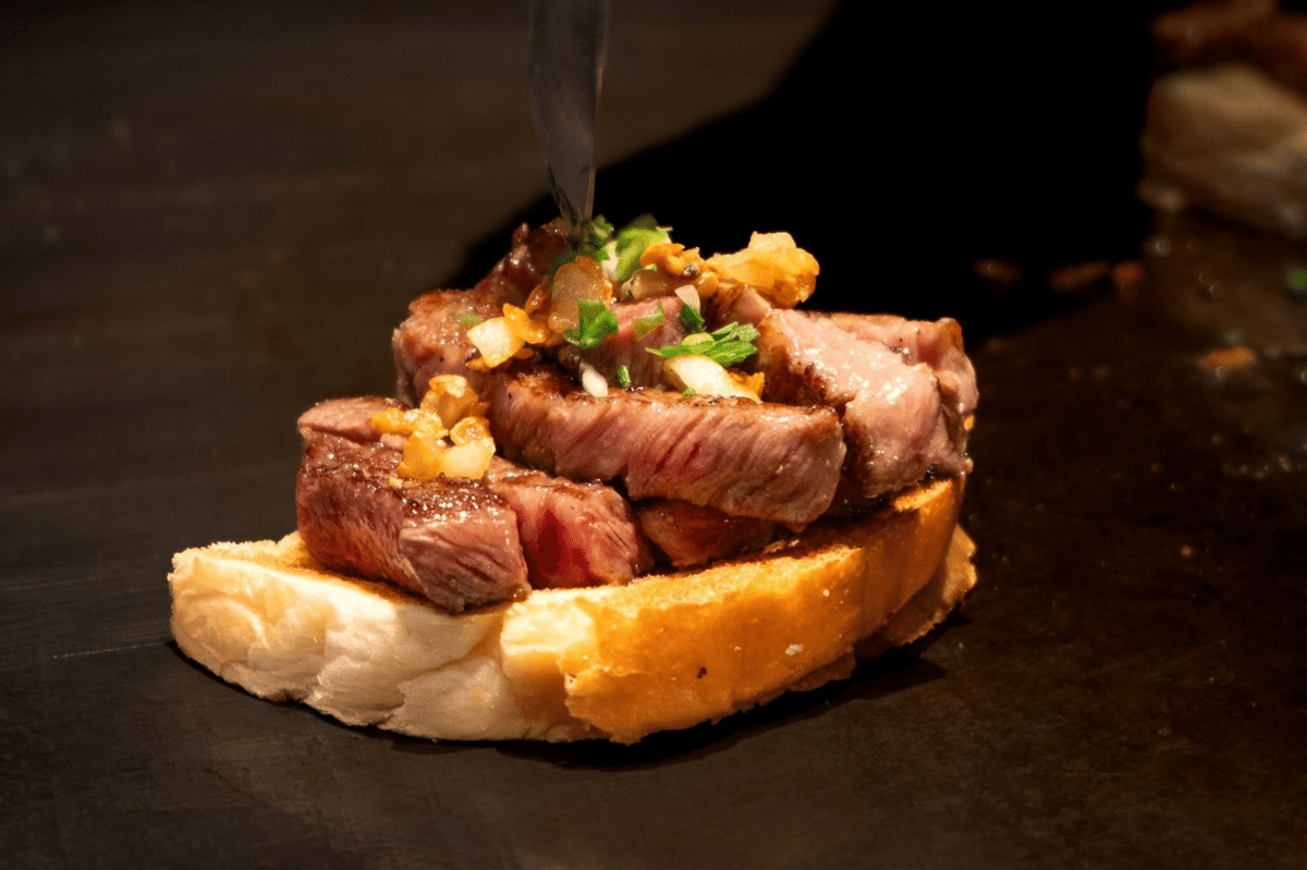 Wagyu katsu sando dengan daging berlapis tepung roti di antara roti putih, disajikan sebagai ilustrasi hidangan.