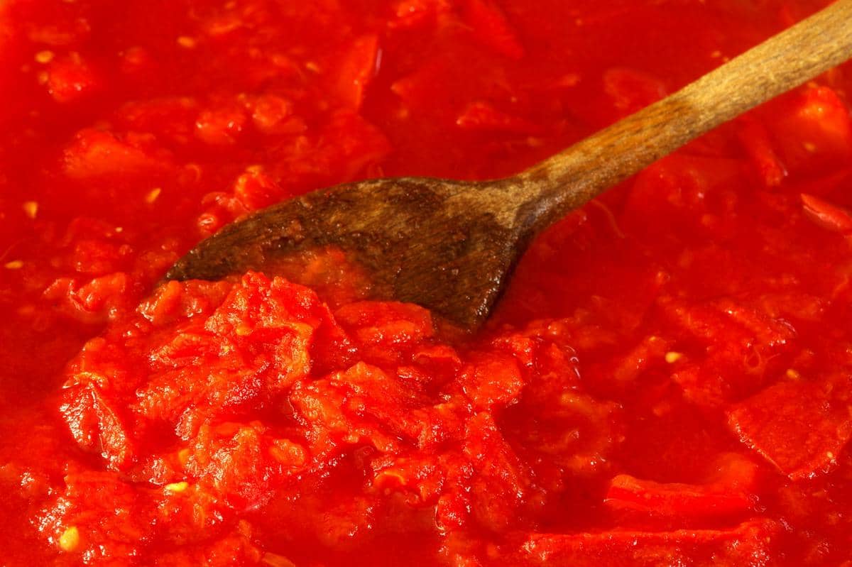 Tomat merah segar, bawang putih, dan rempah disiapkan di atas meja untuk membuat saus tomat rumahan.
