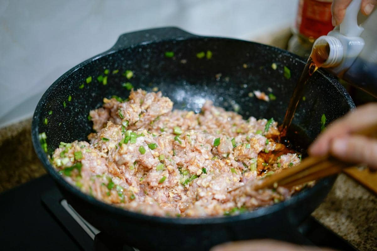 Ilustrasi isian wonton dengan daging cincang dan daun bawang dalam mangkuk, siap digunakan untuk membuat pangsit.