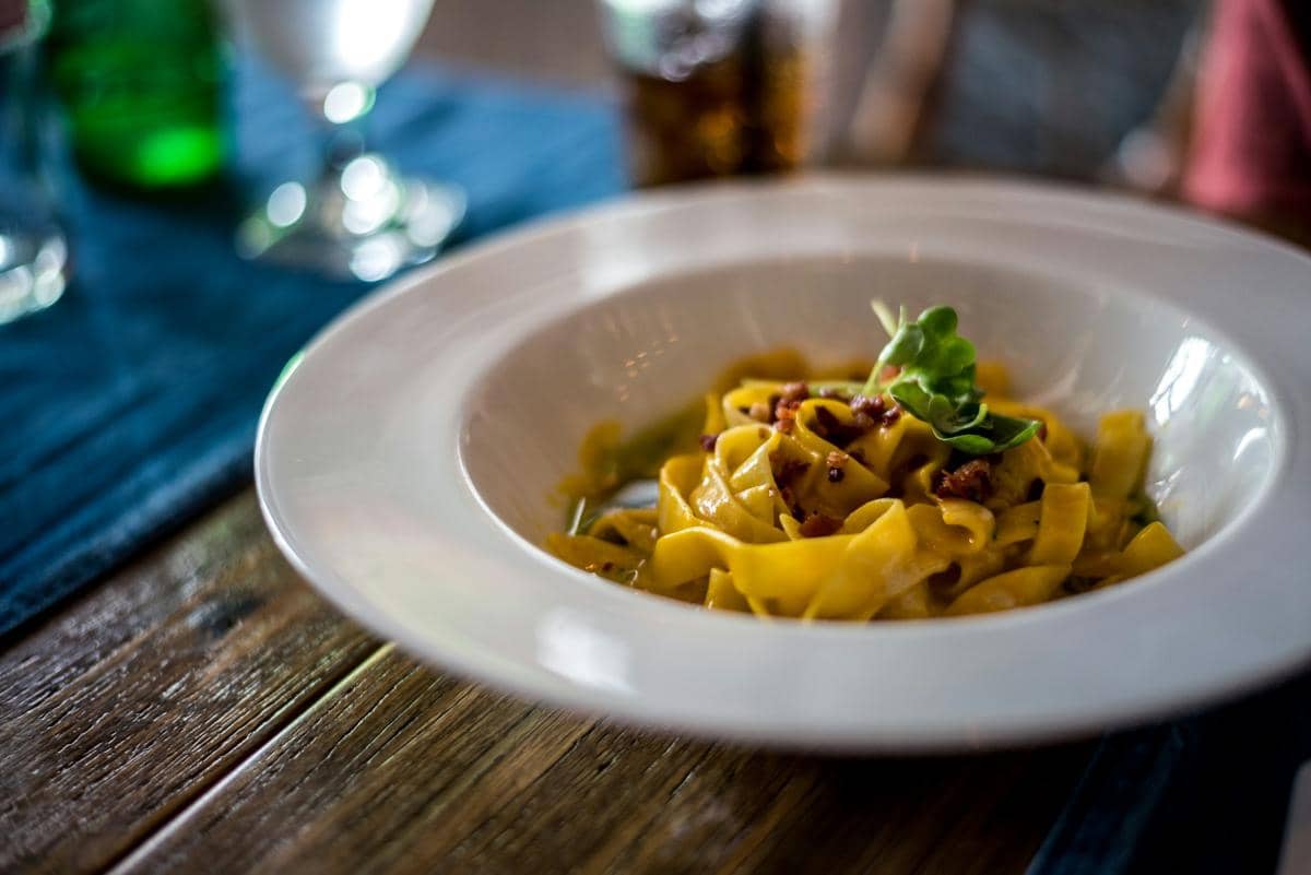 Sepiring pappardelle dengan sosis Italia dalam saus tomat, disajikan di atas meja sebagai ilustrasi hidangan pasta.