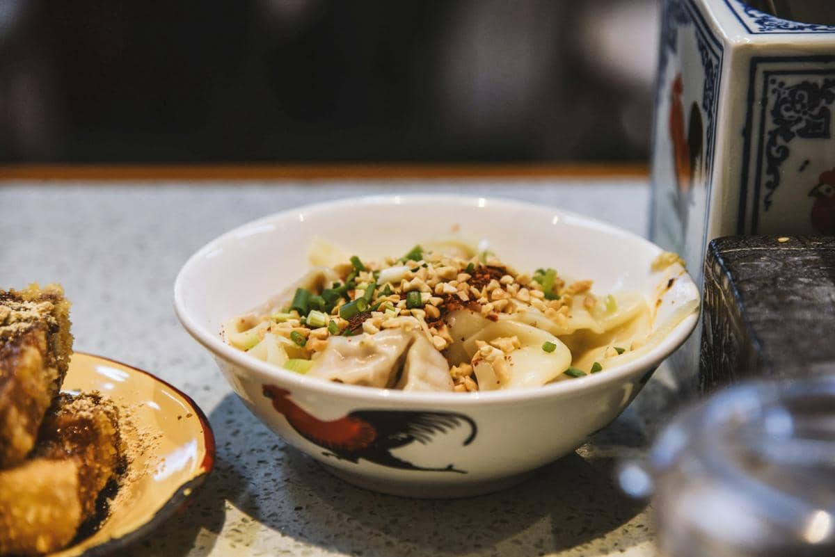 Ilustrasi semangkuk sichuan pork wonton, hidangan pangsit babi khas Sichuan dengan saus pedas berwarna merah.
