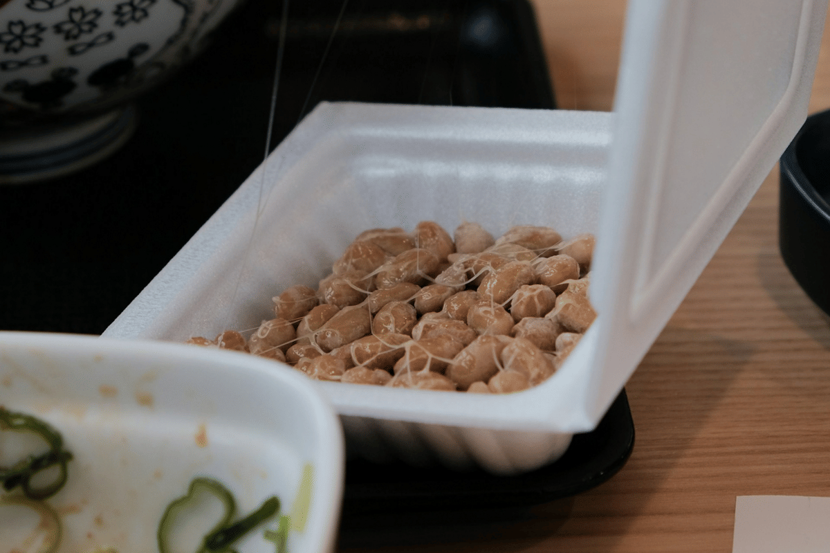 Ilustrasi natto, makanan fermentasi Jepang berbahan kedelai dengan tekstur lengket dan aroma khas.