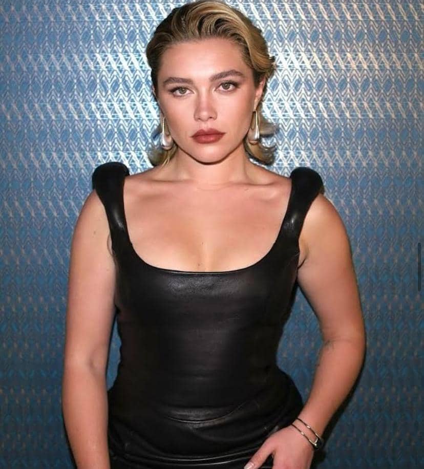 Potret aktris Florence Pugh dengan rambut pirang pendek, mengenakan atasan hitam dan menatap kamera.