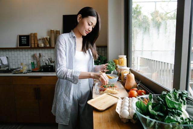 Seorang perempuan memasak di dapur sebagai ilustrasi kegiatan menyiapkan makanan sehari-hari di rumah.